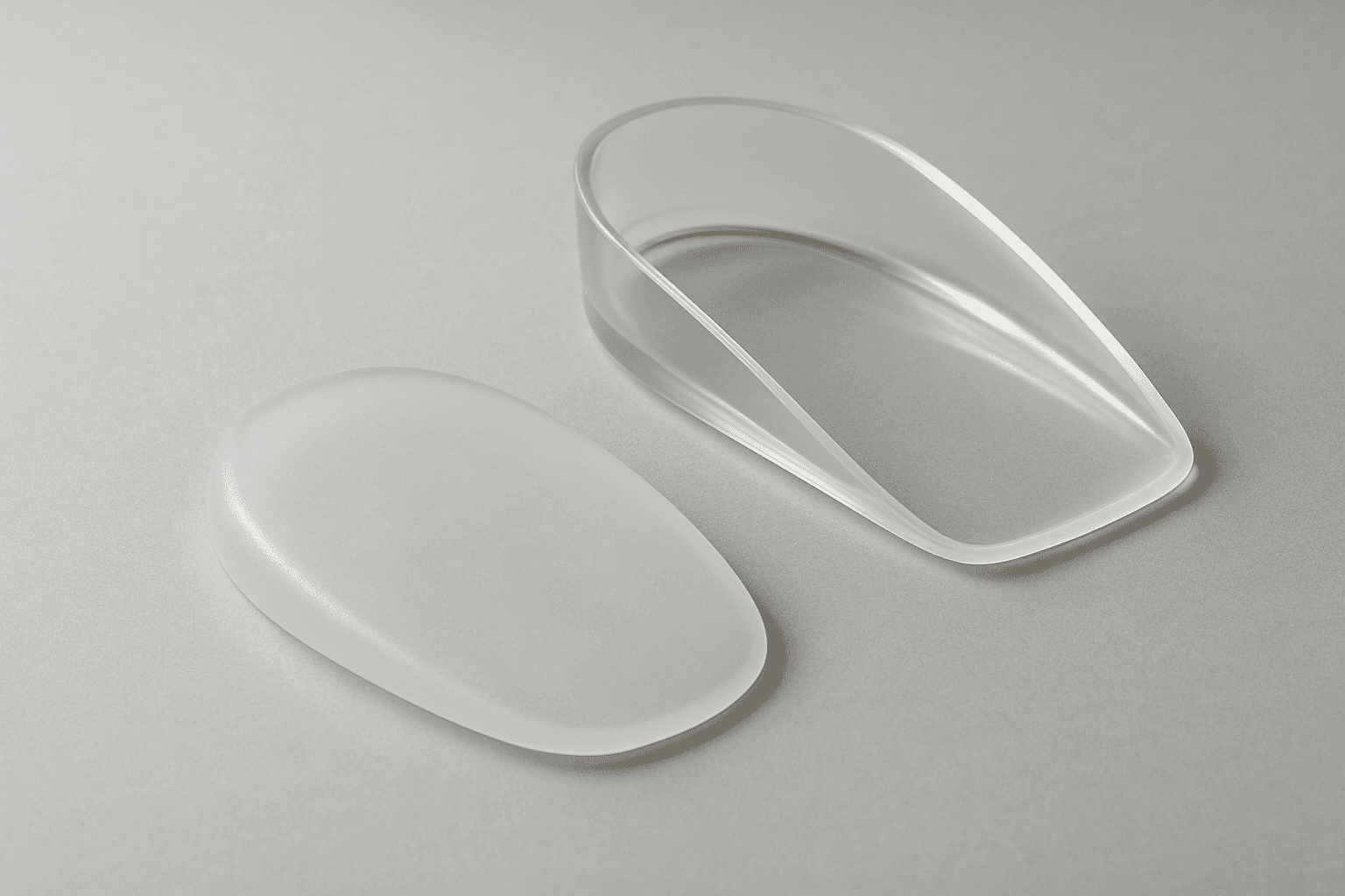 A clear silicone heel cup and a gel heel pad on a pale surface